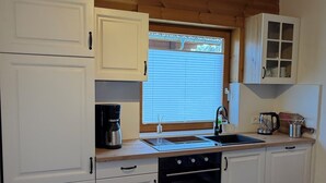 A kitchen with white cabinets, a black oven, a sink, and a window with blinds.