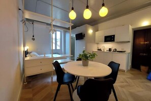 A modern kitchen with white cabinets, a microwave, and a dining area with a round table and chairs. - Central Studio Apartment in Navigli (Milano)