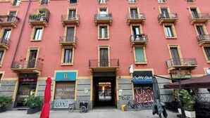 Un immeuble à plusieurs étages doté de balcons, une devanture portant l’inscription « B. » et une enseigne « Café Bar ».