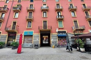 Ein mehrstöckiges Gebäude mit Balkonen, einem Geschäft mit der Aufschrift „B.“ und einem Schild für „Café Bar“.