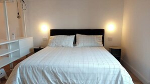 Un lit bien fait, recouvert d’une courtepointe blanche et agrémenté de deux oreillers, avec deux tables de chevet de chaque côté, sur lesquelles sont posées des lampes.