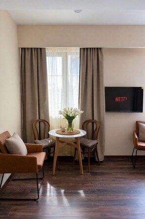 Una sala de estar con un televisor montado en la pared, una mesa redonda con sillas y un sofá.