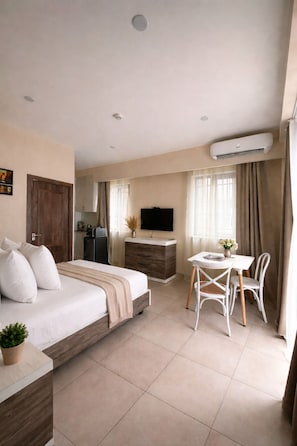 Una habitación de hotel con cama, escritorio, silla, televisor y aire acondicionado.