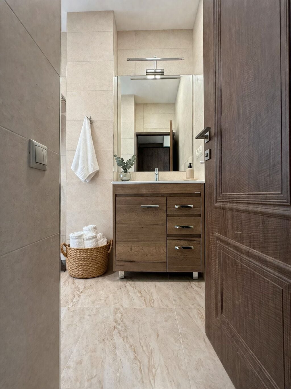 A bathroom with a marble floor, a wooden vanity with drawers, a towel hanging on the wall, and a basket of towels.