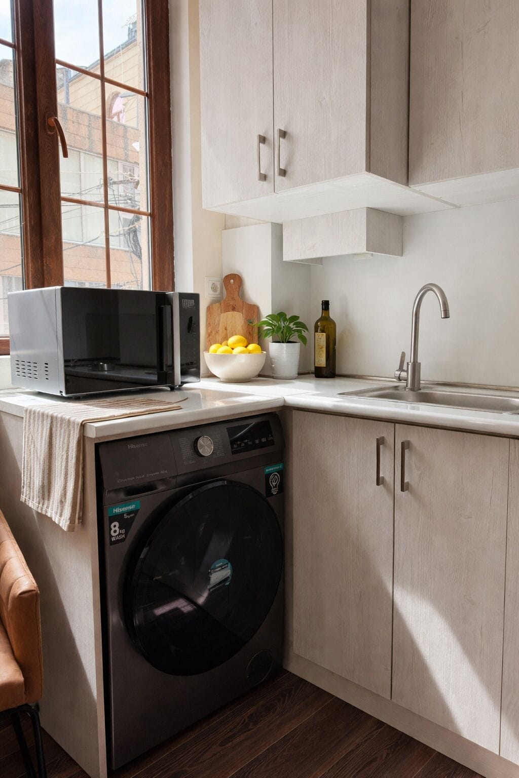 A compact kitchen with a washing machine, a microwave, a sink, and a window.