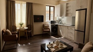 A modern living room with a sofa, a coffee table with pastries, a dining area with chairs, a kitchen with cabinets, and a TV.