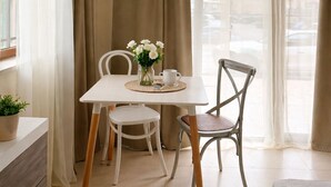 A room with a bed, a table with chairs, a potted plant, and a window with curtains.