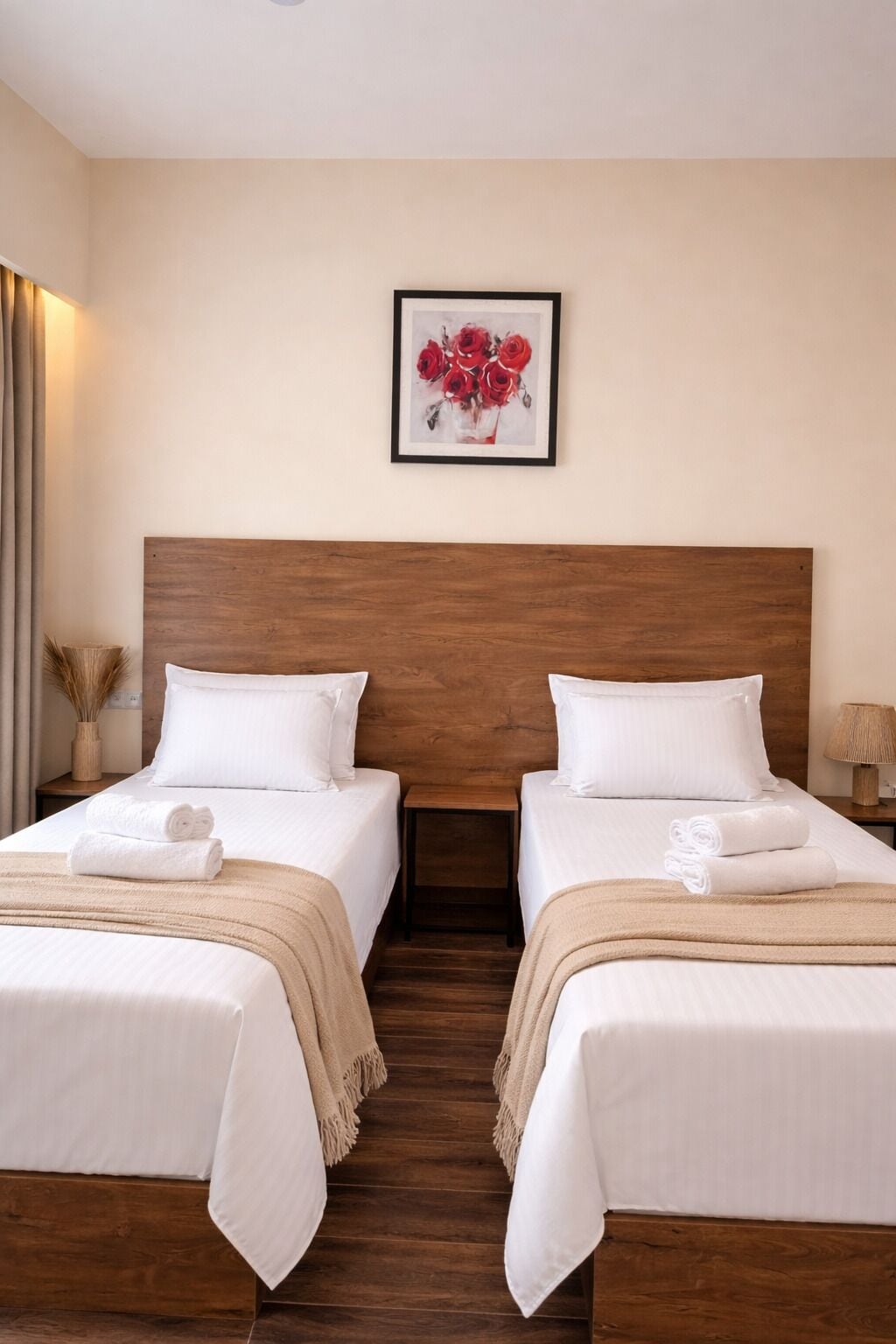 A hotel room with two beds, a wooden headboard, a framed picture of red roses, and a lamp on the nightstand.