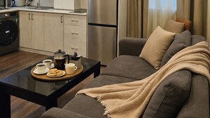 A modern living room with a sofa, a coffee table, and a kitchen area with cabinets and a refrigerator.