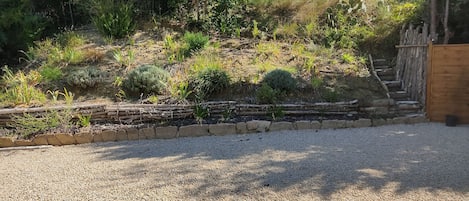 Un jardín con un sendero de grava, escalones de madera y diversas plantas.