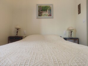 A bedroom with a large bed, two bedside tables with lamps, a framed picture on the wall, and a small wall clock. - Rent F1 in Luberon near 30 km from Aix en Provence, Cavaillon, (Cadenet)
