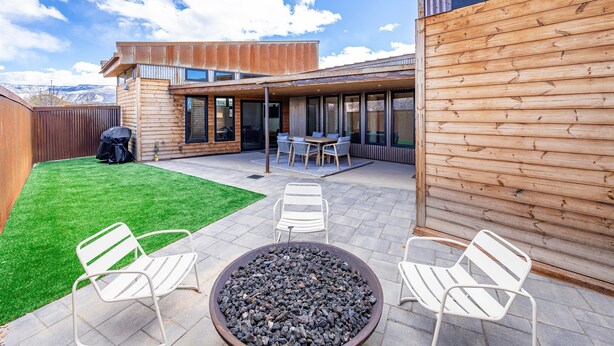 Een modern terras buiten met een vuurkorf, een zithoek en uitzicht op de bergen.