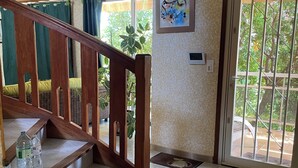 Un escalier avec des rampes en bois, un sol carrelé, une porte avec une fenêtre et un thermostat fixé au mur.