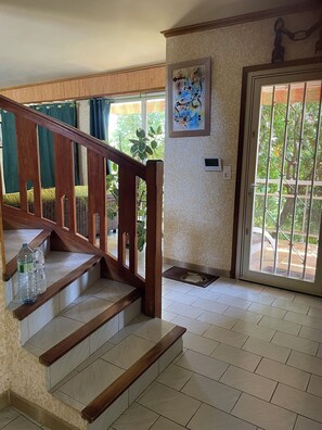 Eine Treppe mit Holzgeländern, Fliesenboden, einer Tür mit Fenster und einem an der Wand montierten Thermostat.