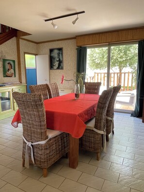 Ein Essbereich mit rotem Tisch, Korbstühlen, einer Blumenvase und Blick ins Freie.