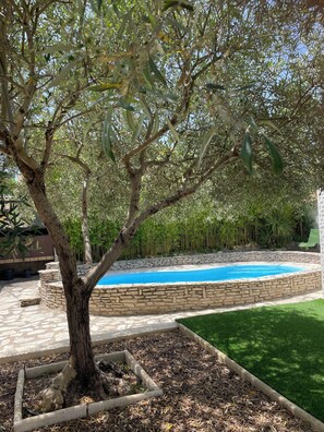 Ein von Bäumen gesäumter Außenbereich mit Swimmingpool, Steintreppe und Rasenfläche.