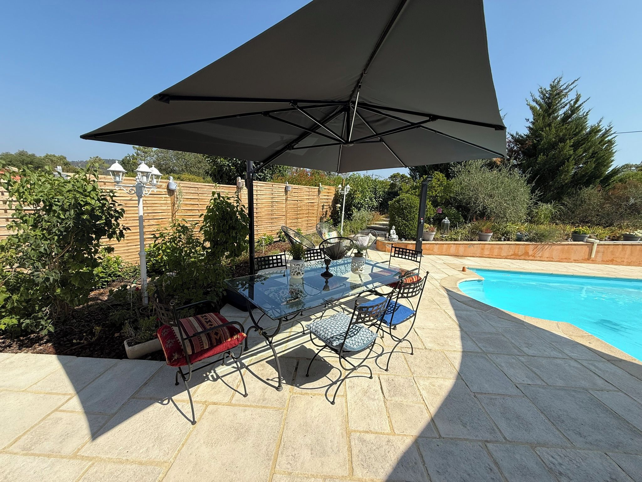 En udendørs terrasse med pool, omgivet af et træhegn, stenbelægning og havemøbler.