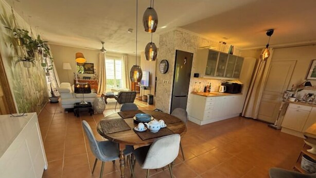 Uma sala ampla com uma mesa de jantar, cadeiras, um sofá e uma cozinha ao fundo.