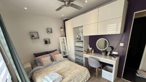 Quarto com cama, escrivaninha, cadeira, ventilador de teto e guarda-roupa.