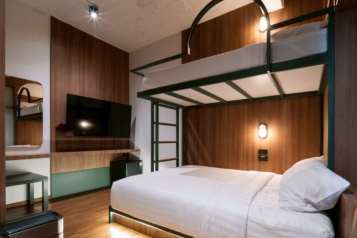 Ein Stockbett mit Fernseher, Schreibtisch und Spiegel in einem Zimmer mit Holzwänden und einem Deckenlüfter.