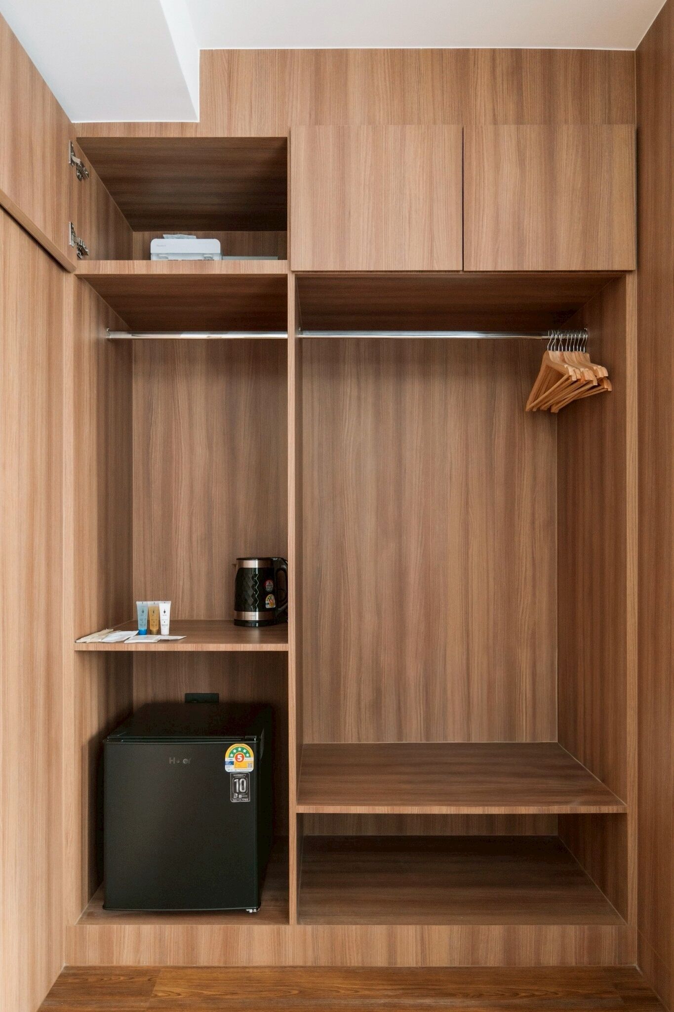 A wooden wardrobe with multiple shelves, a hanging rack, and a small black refrigerator.