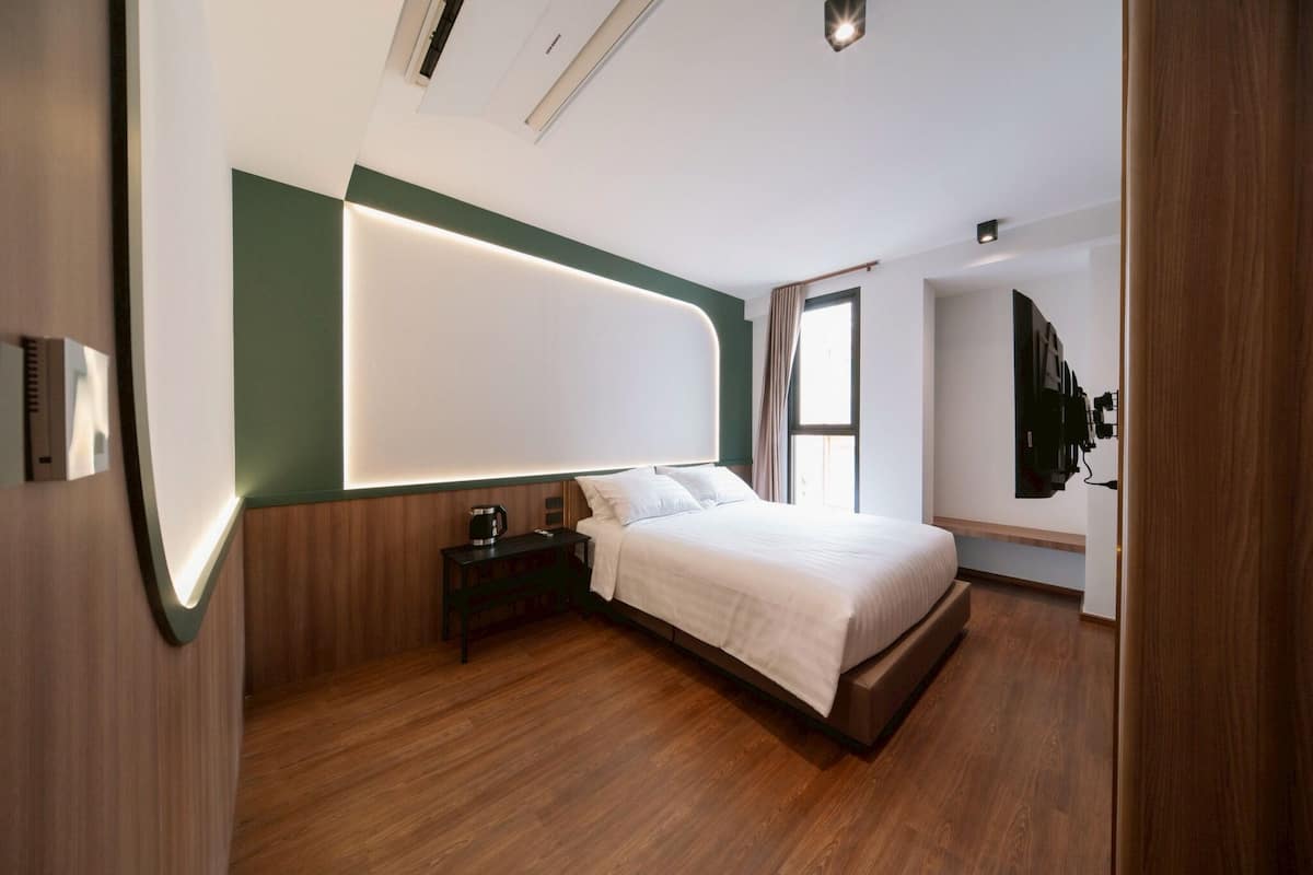 Ein modernes Hotelzimmer mit Holzboden, einem Bett mit weißer Bettwäsche, einem Nachttisch mit Kaffeemaschine und einem an der Wand befestigten Fernseher.
