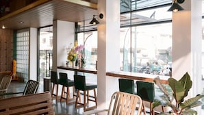Un intérieur moderne avec un banc en bois, des chaises vertes, un coin repas et de grandes fenêtres.