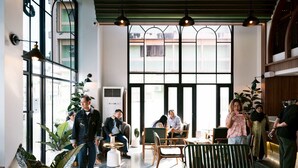 Un espace intérieur vaste et lumineux, avec de grandes fenêtres, des coins salon et des plantes en pot.