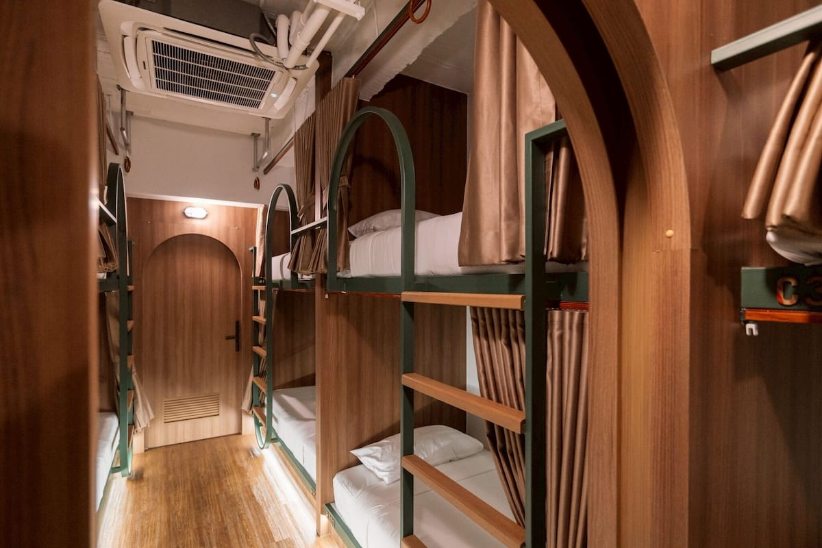 Ein schmaler Korridor mit Etagenbetten, Holzwänden und einem Deckenventilator.