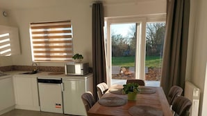A compact kitchen with a microwave, sink, and dishwasher. A dining table with four chairs and a potted plant is in the foreground. - Stork country (Brugelette)