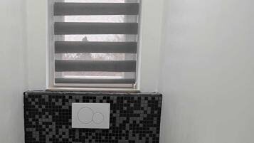 Een compacte, moderne badkamer met toilet, wastafel en een raam met zonwering.