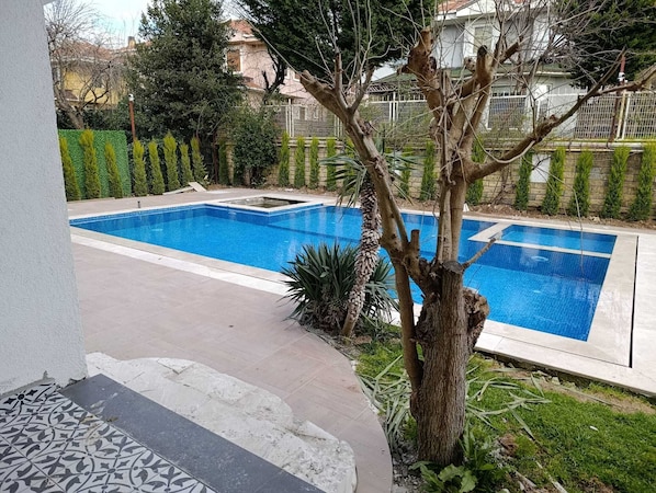 A rectangular swimming pool with a tiled border, surrounded by a paved patio area.