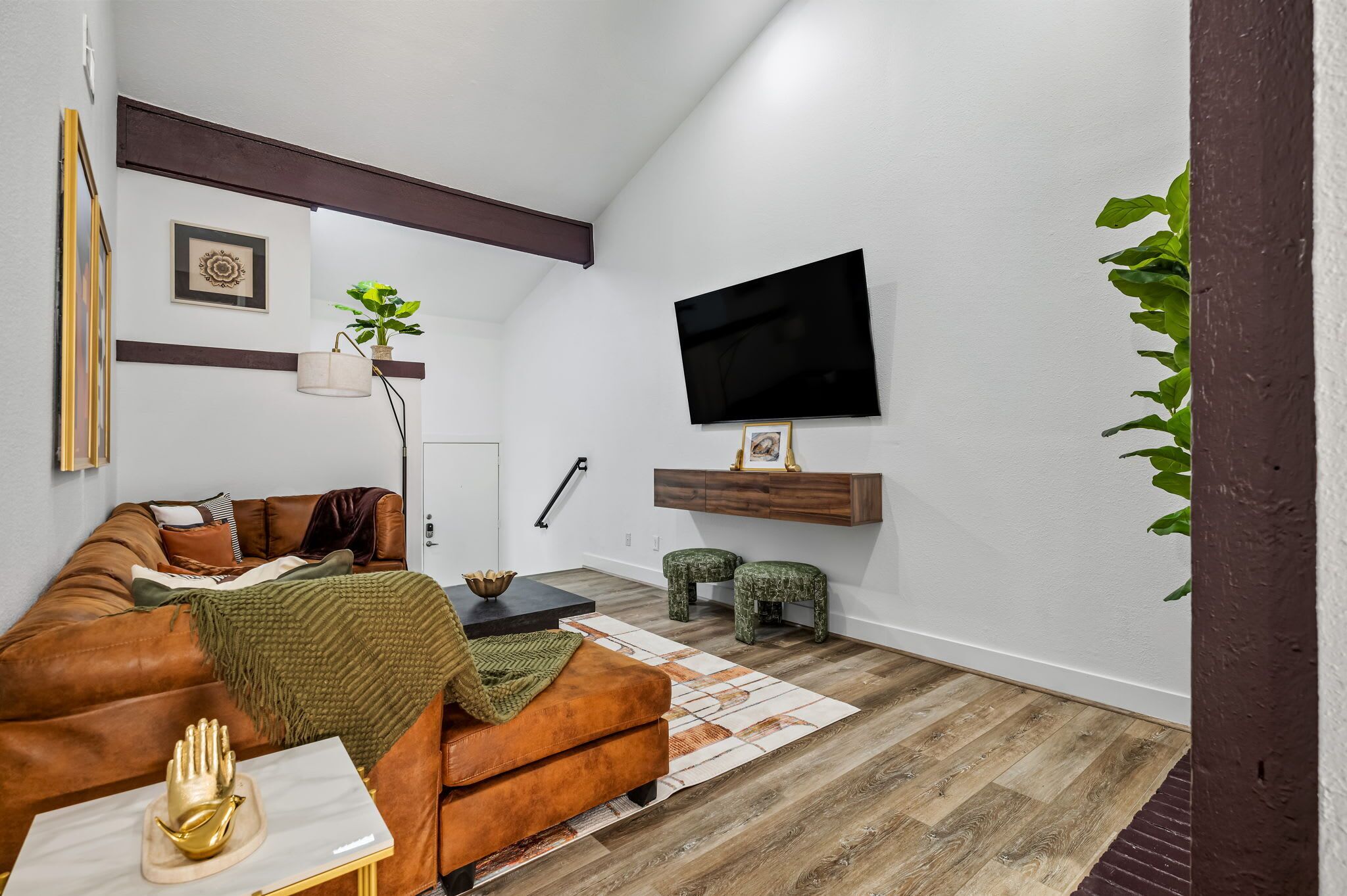 Een woonkamer met een bruine leren bank, een witte salontafel, een flatscreen-televisie aan de muur en een houten vloer.