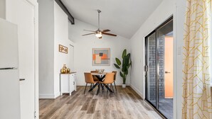 Eine moderne Küche mit Essbereich, ausgestattet mit einem Deckenventilator, einem Esstisch mit Stühlen, einem Blumentopf und Blick durch eine Glastür.