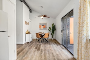 A modern kitchen with a dining area, featuring a ceiling fan, a dining table with chairs, a potted plant, and a view through a glass door. - The Orange Doors - Two Homes - Plunge Pool (Austin)