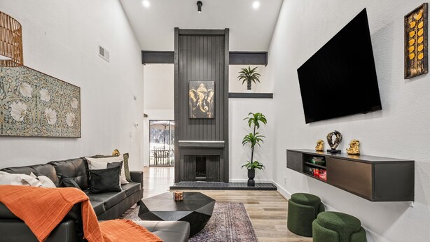 Una sala de estar moderna con un sofá de cuero negro, una mesa de centro, una chimenea y un televisor montado.