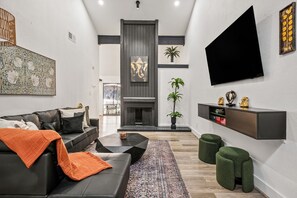 Ein modernes Wohnzimmer mit einem schwarzen Ledersofa, einem Couchtisch, einem Kamin und einem Wand-Fernseher.