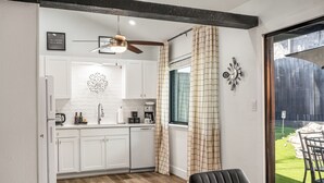 Una cocina compacta con armarios blancos, ventilador de techo y ventana con cortinas.