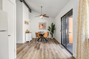 A modern kitchen with a dining area, featuring a ceiling fan, a dining table with chairs, a potted plant, and a view through a glass door. - The Orange Door - Unit A - Heated Plunge Pool (Austin)