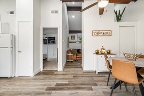 Eine moderne Küche mit Essbereich, ausgestattet mit Holzboden, weißen Schränken und einer Kaffeebar-Beschilderung.