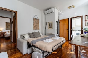 Ein Schlafzimmer mit Bett, Sofa, Esstisch und einer durchgehenden Tür erkennbaren Küchenzeile.
