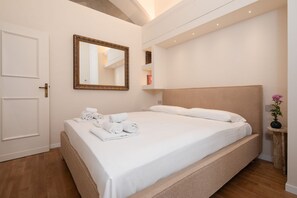 A neatly made bed with rolled towels, a large mirror, and a small table with a vase. - Signoria Design Retreat (Florence)