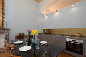 A modern dining area with a black table set for four, a vase with flowers, and a kitchen with an oven and a sink. - Signoria Design Retreat (Florence)