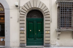 A green double door with a decorative arch above it, a window with metal bars, and a plaque with a number on the wall. - Signoria Design Retreat (Florence)
