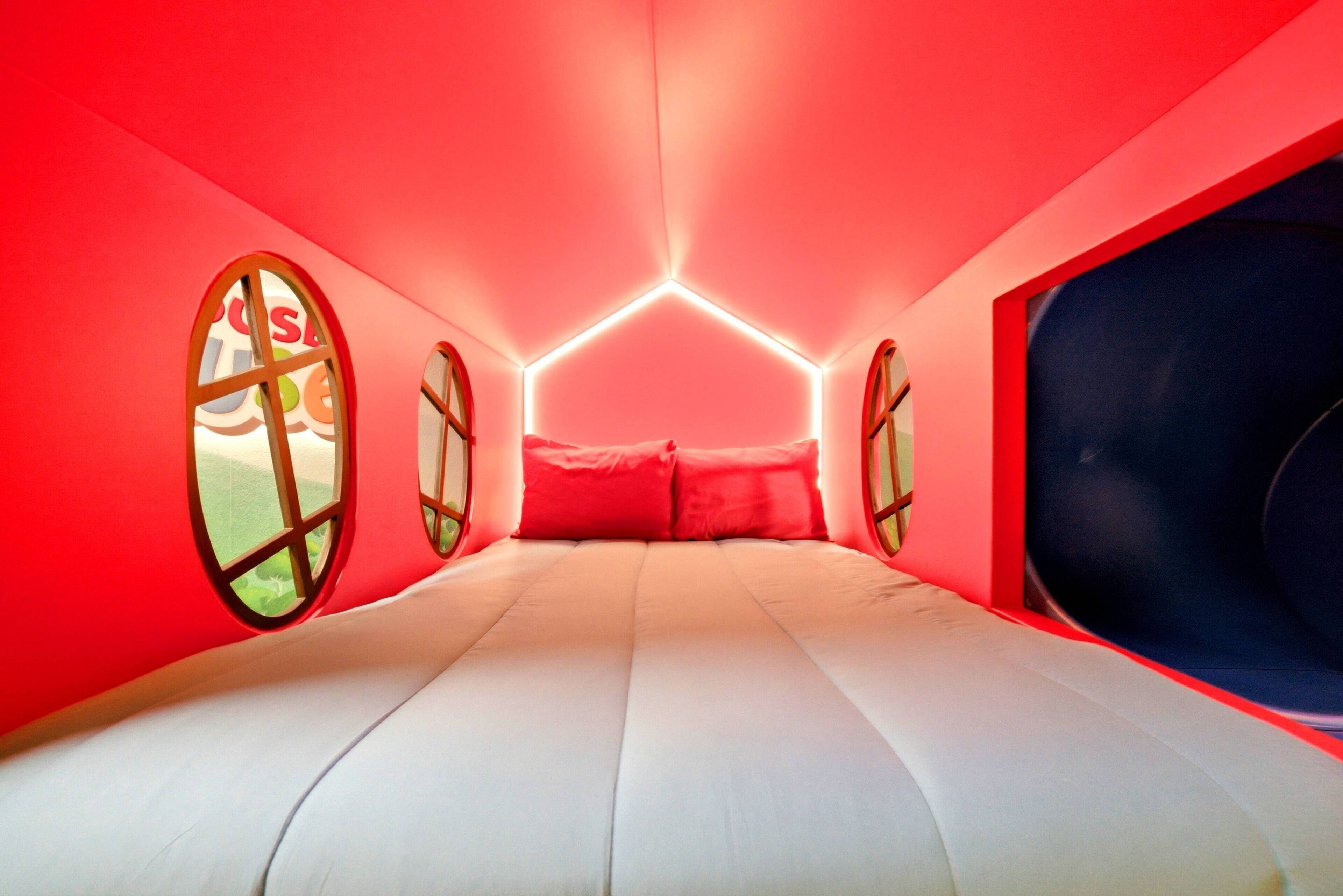 Step into a vibrant hideaway featuring playful red walls and charming circular windows that invite in natural light. The cozy bedding offers a restful spot to unwind, while the unique design adds a whimsical touch to your stay.
