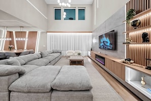 Unwind in this chic living room with a roomy gray sectional perfect for gatherings. Enjoy the inviting atmosphere from the modern entertainment unit and sleek lighting, enhanced by large windows that fill the space with natural. - 7BR house with game room near Disney (Kissimmee)