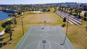 Ein Basketballplatz im Freien mit Netz, umgeben von Gras und Palmen.