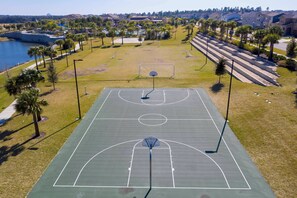 An outdoor basketball court with a net, surrounded by grass and palm trees. - 7BR house with game room near Disney (Kissimmee)