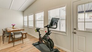 Quarto com uma mesa de jantar, cadeiras, uma bicicleta de exercício Peloton e uma porta com janela.