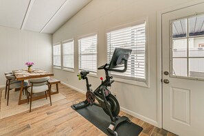 Ein Zimmer mit Esstisch, Stühlen, einem Peloton-Trainingsgerät und einer Tür mit Fenster.